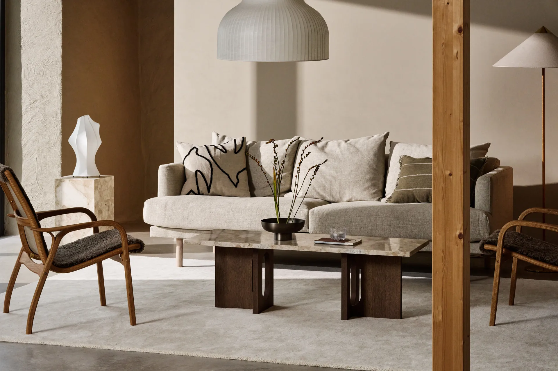 En koselig stue med lys beige sofa, marmorsalongbord, tre lenestoler og en ribbet taklampe.