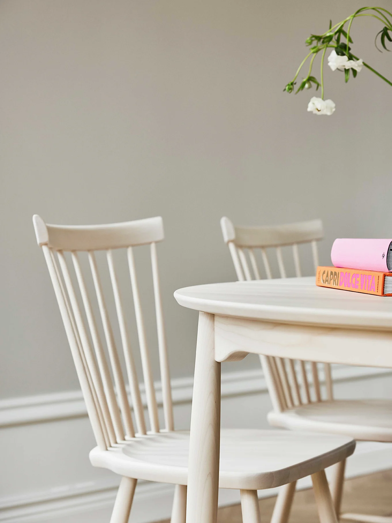 Oversiktsbilde av et ovalt spisebord i lyst tre med en utskåret treskål og tre stoler med mørkebrune seter på et brunt teppe.