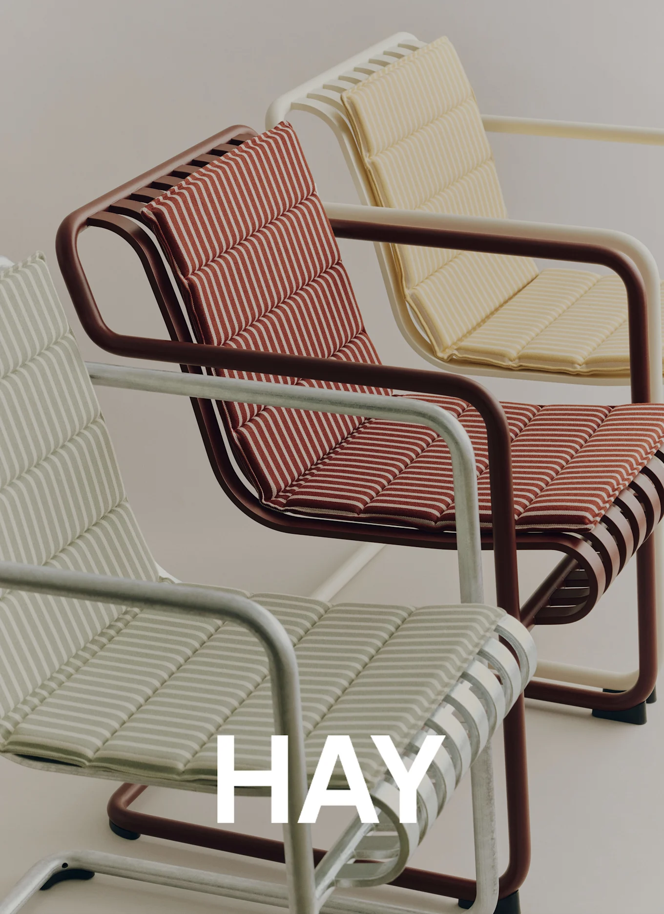 Tre moderne stoler med stripete puter: lysegrønn, rød og gul, på lys bakgrunn. Merkenavn HAY synlig.