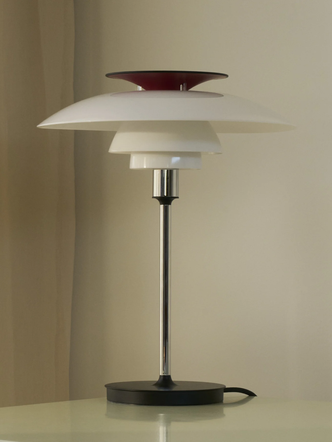 En bordlampe med hvite, lagdelte skjermer og en rød topp, på en sølvfarget stang og sort base.