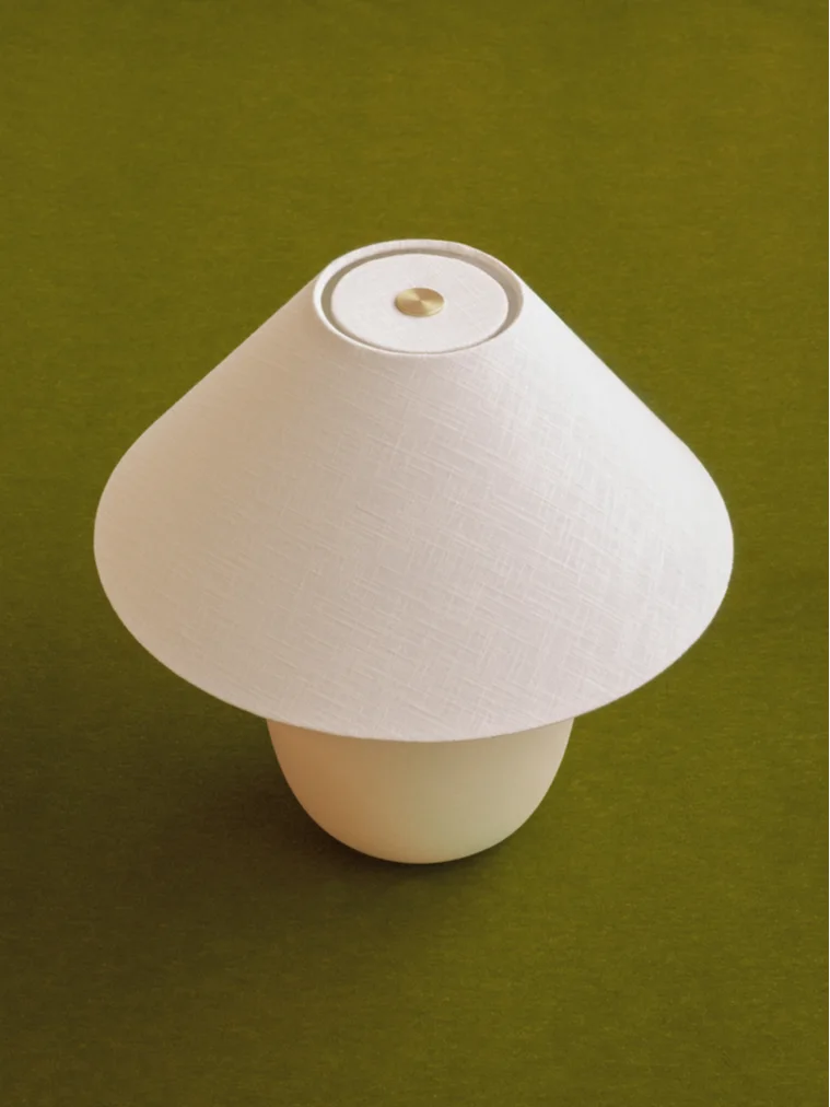 Soppformet bordlampe med hvit stoffskjerm og lys base, med en messingdetalj på toppen.