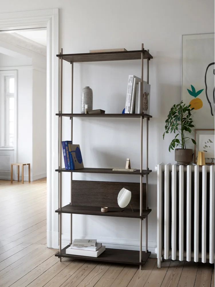 Mørkt trehyllesystem med fire hyller, lyse metallstolper, bøker og dekorasjoner i et lyst rom.
