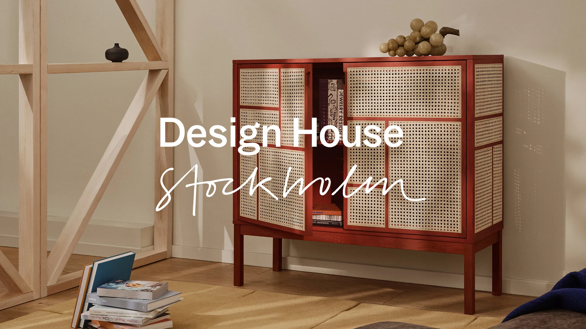 Teksten Design House Stockholm over et trebord med moderne hvitt servise, gul frukt og blomster, mot en lys trevegg.