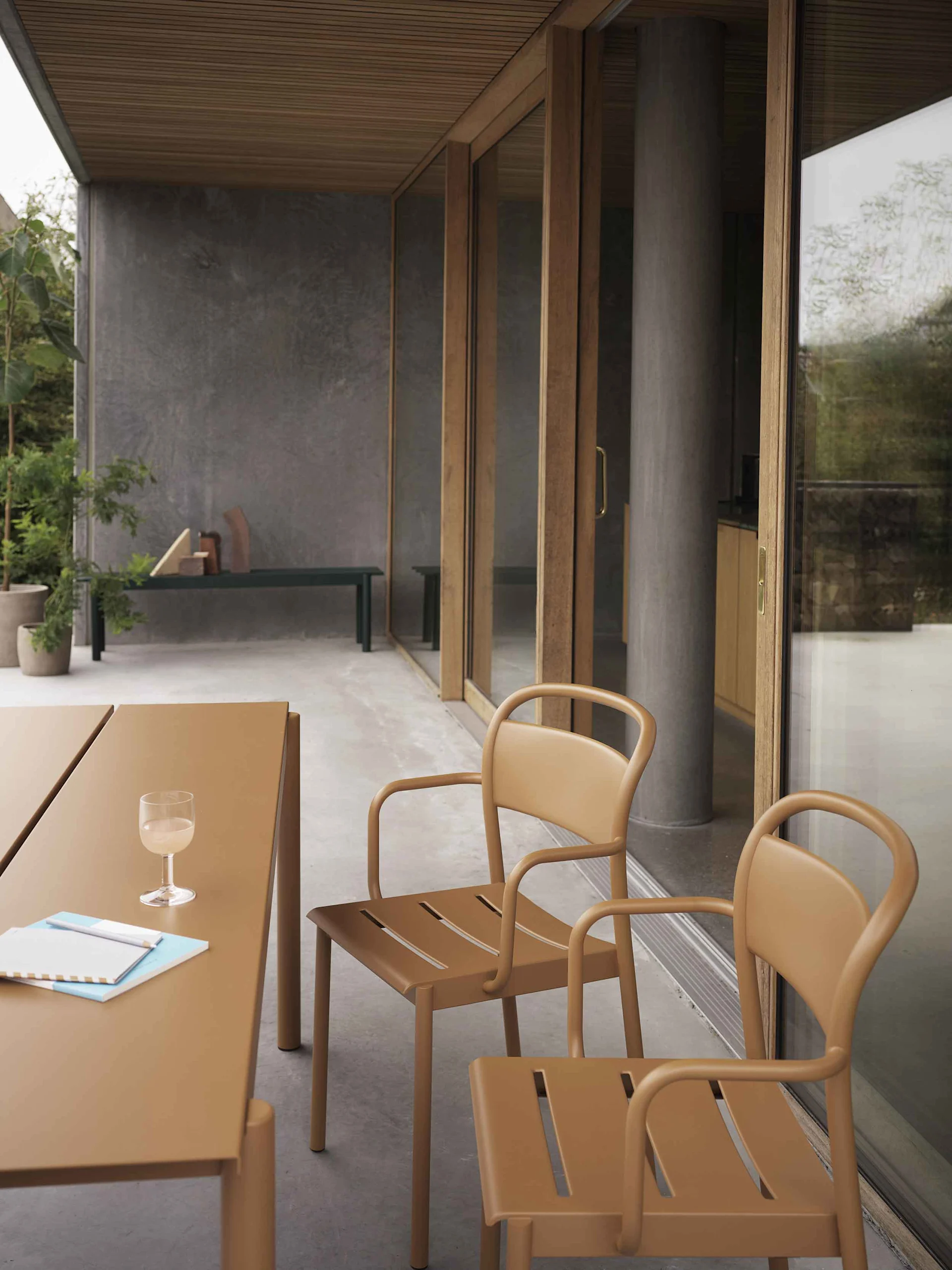 Uteplass med brunt/tan bord og to matchende stoler med avrundede rammer og spalteåpninger i setet, foran skyvedører i glass.