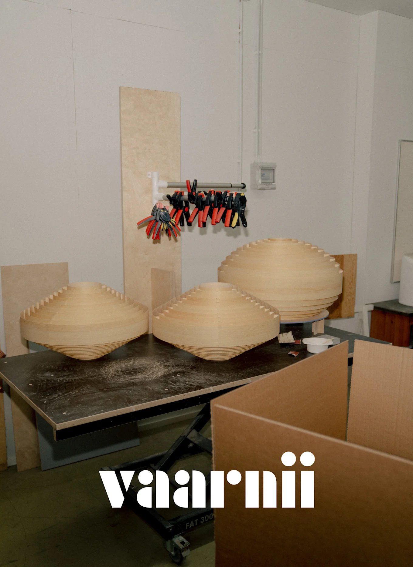 Tre store, lyse, lagdelte treobjekter med konisk form på en mørk arbeidsbenk i et Vaarnii-verksted.