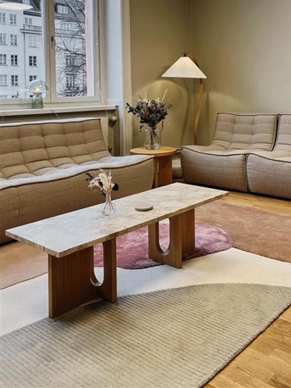 En moderne stue med lys grå sofa, beige teppe, to mørkebrune bord og to ulike lamper.