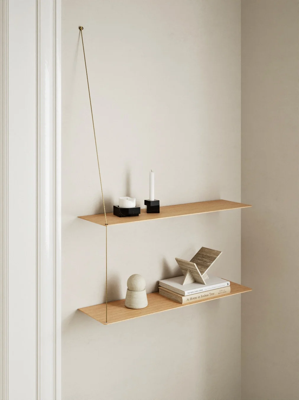 To minimalistiske hyller i lyst tre, hengt opp med en tynn messingstang. Øverste hylle har to hvite lys. Nederste hylle har bøker og dekor.
