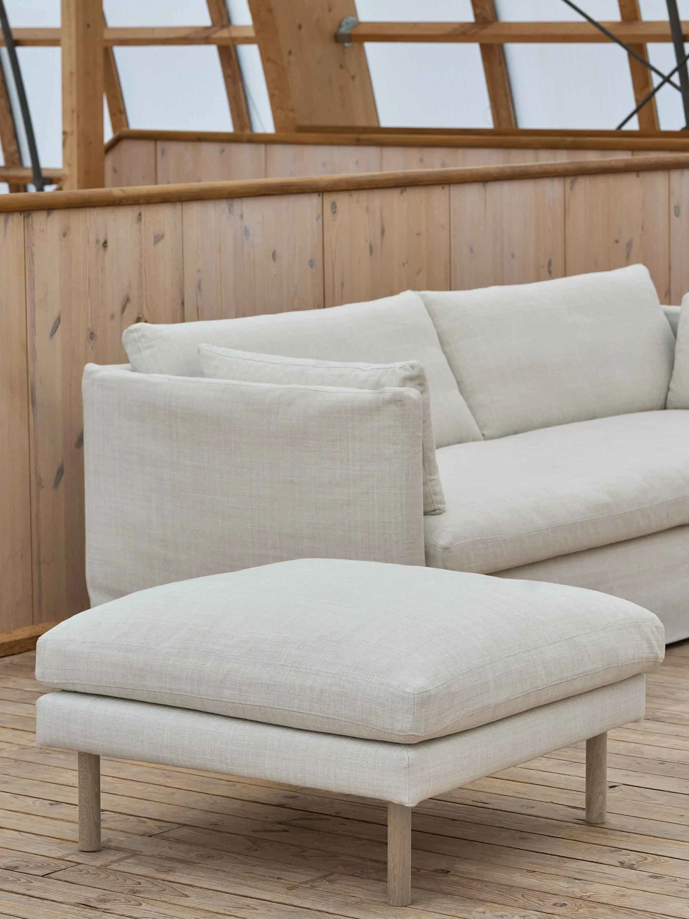 En lys beige polstret sofa og matchende puff på et tredekk.