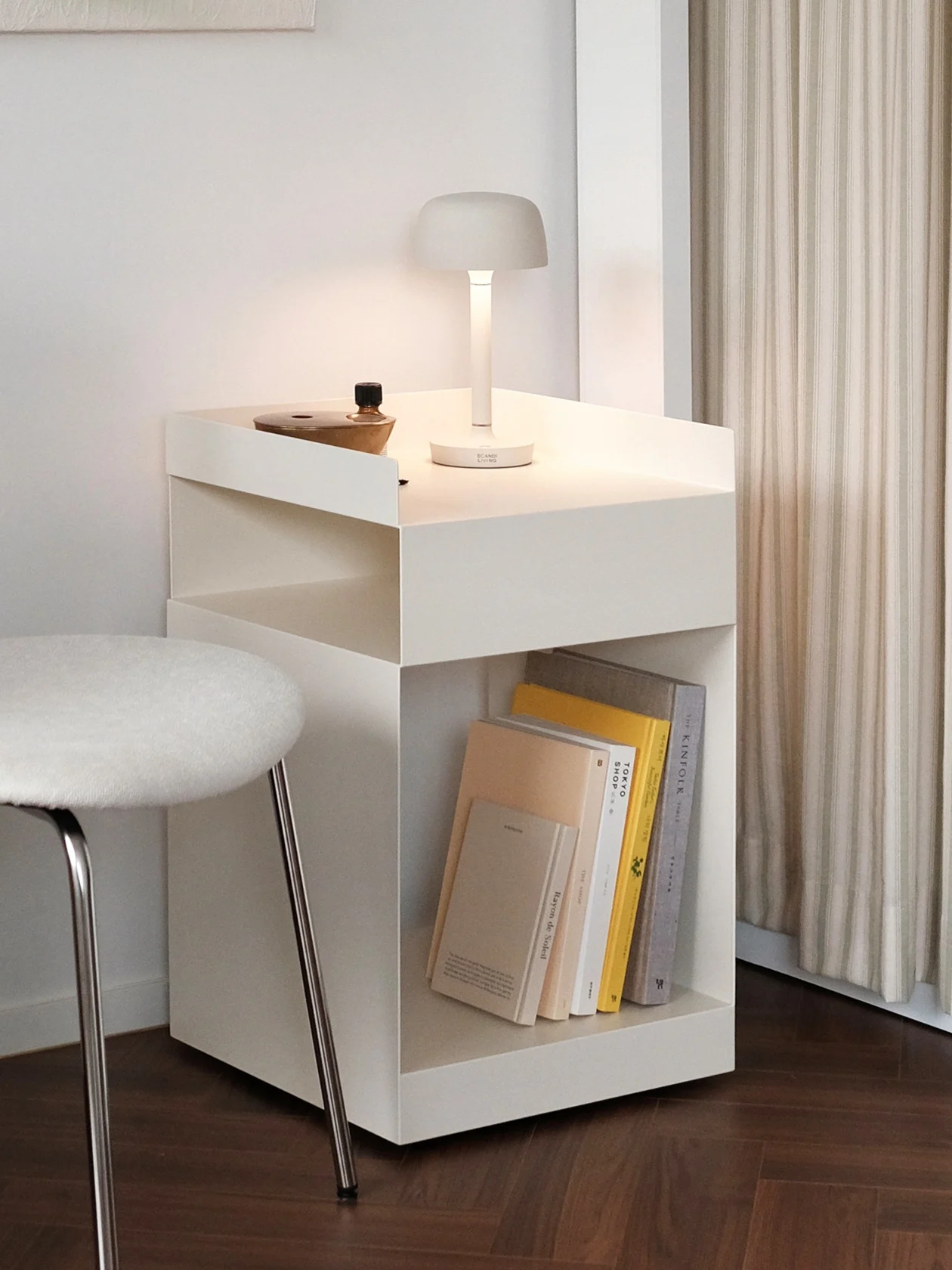 Moderne hjørne med hvit vegg, lyst abstrakt maleri, stol, sidebord med lampe, grønn hengeplante og stripete gardiner.