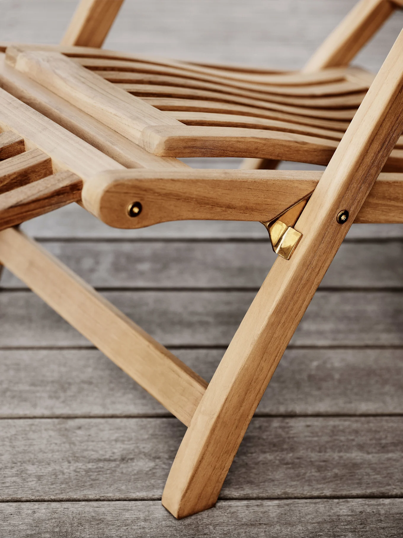 Nærbilde av en foldbar stol i tre med spiler og messingdetaljer på et tregulv.