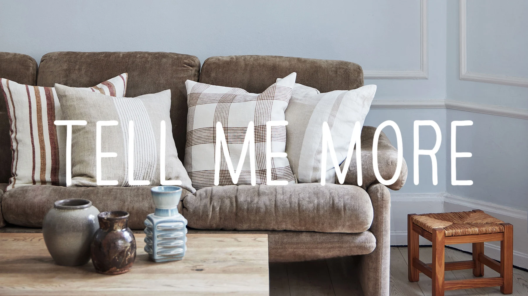 Brun sofa med mønstrede linputer, salongbord med tre keramikkvaser og en liten flettet krakk.