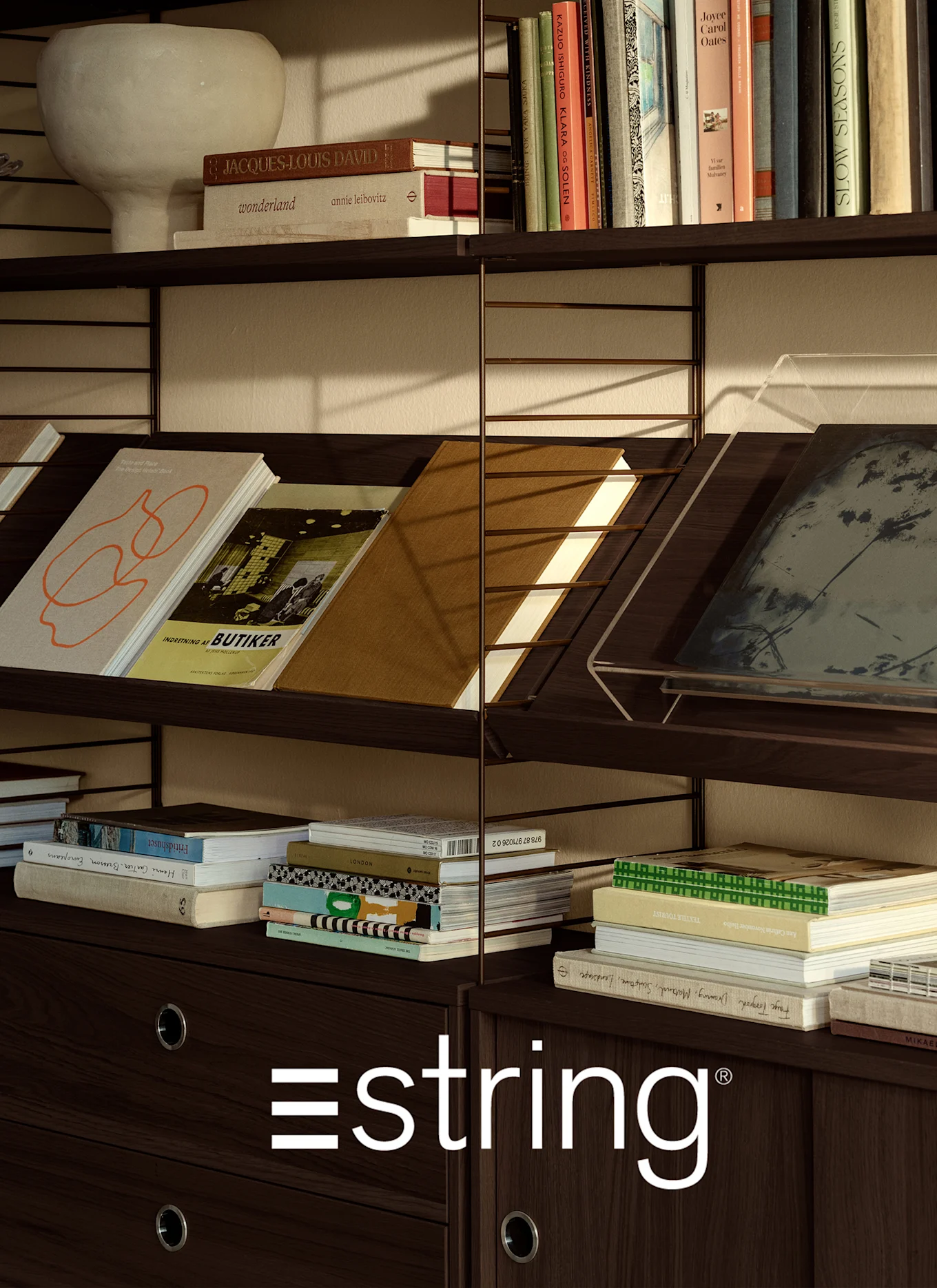 Mørkebrun trehylle med diverse bøker, en lys vase og den hvite 'estring'-logoen nederst.