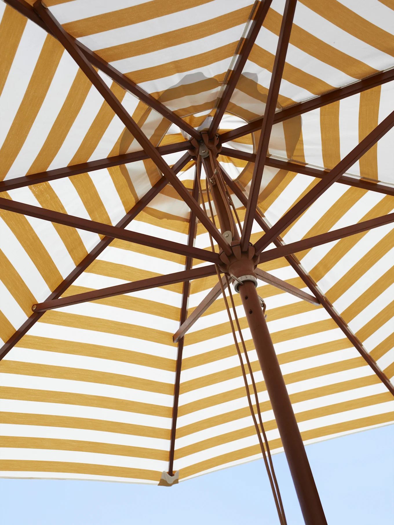 Undersiden av en gul- og hvitstripet parasoll, som viser trestammen mot en blå himmel.