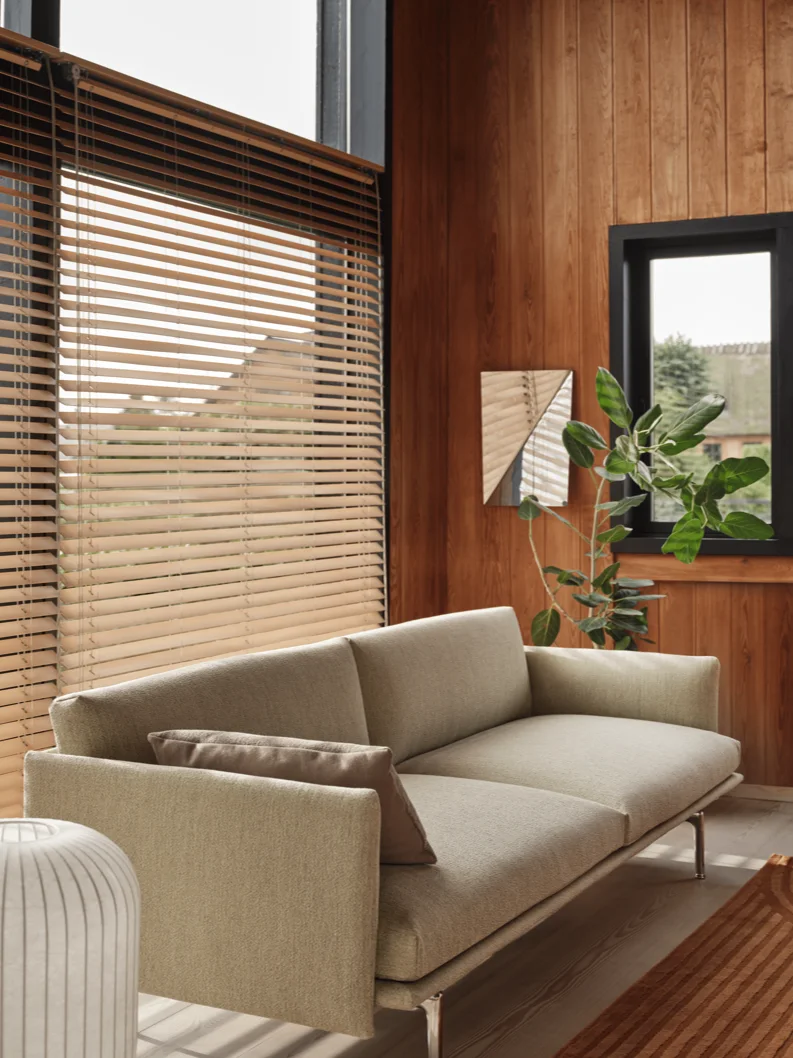 Moderne stue med lys sofa, trepanel på veggene, store vinduer med lyse trepersienner, grønn plante og et dekorativt speil.